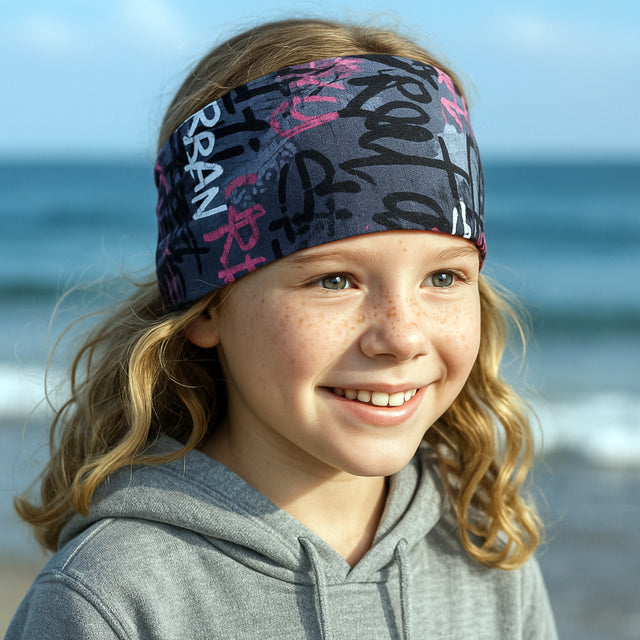 Mädchen am Strand trägt das Wollhuhn Elastisches Öko Stirnband – ein handgemachtes, vielseitiges Jersey-Accessoire aus weicher Bio-Baumwolle, ideal für Outdoor-Aktivitäten.