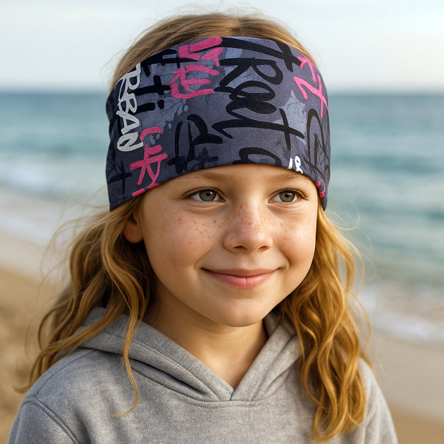 Mädchen am Strand trägt Wollhuhn Elastisches Öko Stirnband aus doppellagigem Jersey, ideal für Outdoor-Aktivitäten und sportliche Looks.