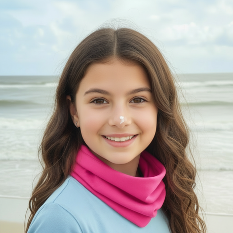 Mädchen am Strand, trägt Wollhuhn Leichtes Lockeres Öko Jersey Halstuch in Pink, ideal für Kinder, handgefertigt, schützt vor Wind und Sonne, perfekt für Übergangszeiten.