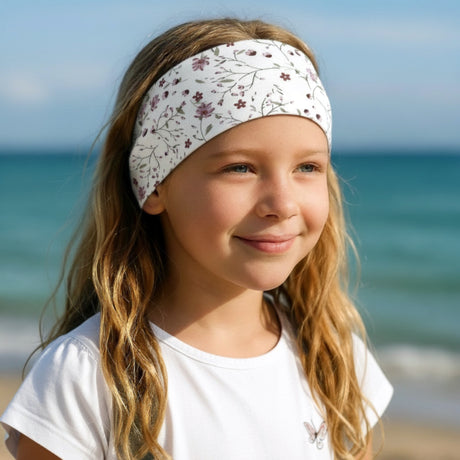 Ein junges Mädchen am Strand trägt ein Wollhuhn Elastisches Öko Stirnband aus Bio-Baumwolle mit Blumenmuster, perfekt für Freizeitaktivitäten und Outdoor-Abenteuer.