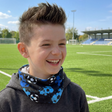 Junge mit Wollhuhn Öko Jersey Halstuch, Fußballmuster in Blautönen, auf Fußballfeld; lächelnd, trägt Hoodie, zeigt lockeres, wendbares Design, ideal für Übergangszeiten.