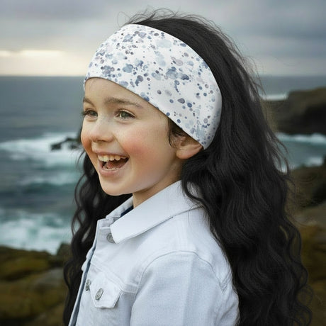 Junges Mädchen am Felsstrand trägt Wollhuhn Elastisches Öko Stirnband, zweilagig breit, mit Aquarellsprenkeln; handgemacht aus Bio-Baumwolle, ideal für Outdoor-Aktivitäten.