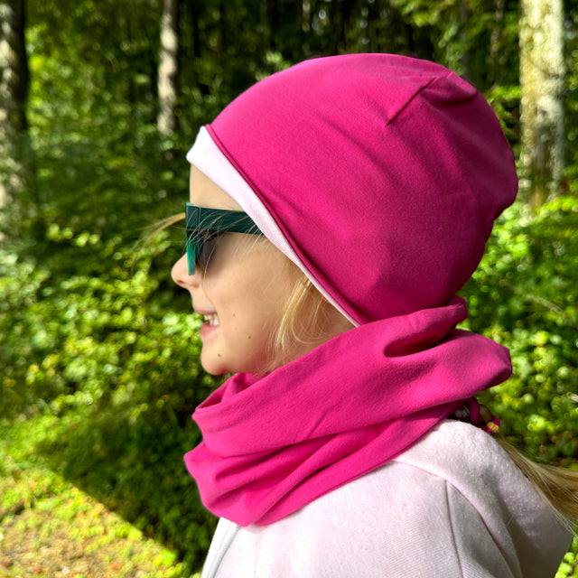 Mädchen mit pinkem Hut und Sonnenbrille trägt den Wollhuhn LONG Loop in Einfarbig Pink, ideal für Komfort und Schutz, handgemacht in Deutschland.