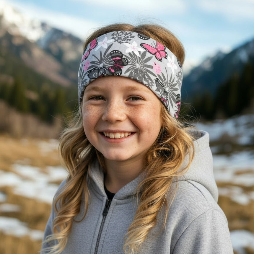 Junges Mädchen mit Wollhuhn Elastisches Öko Stirnband, graues Design mit Schmetterlingen, in Bergwiese. Ideal für Outdoor-Aktivitäten, handgefertigt aus Bio-Baumwolle.