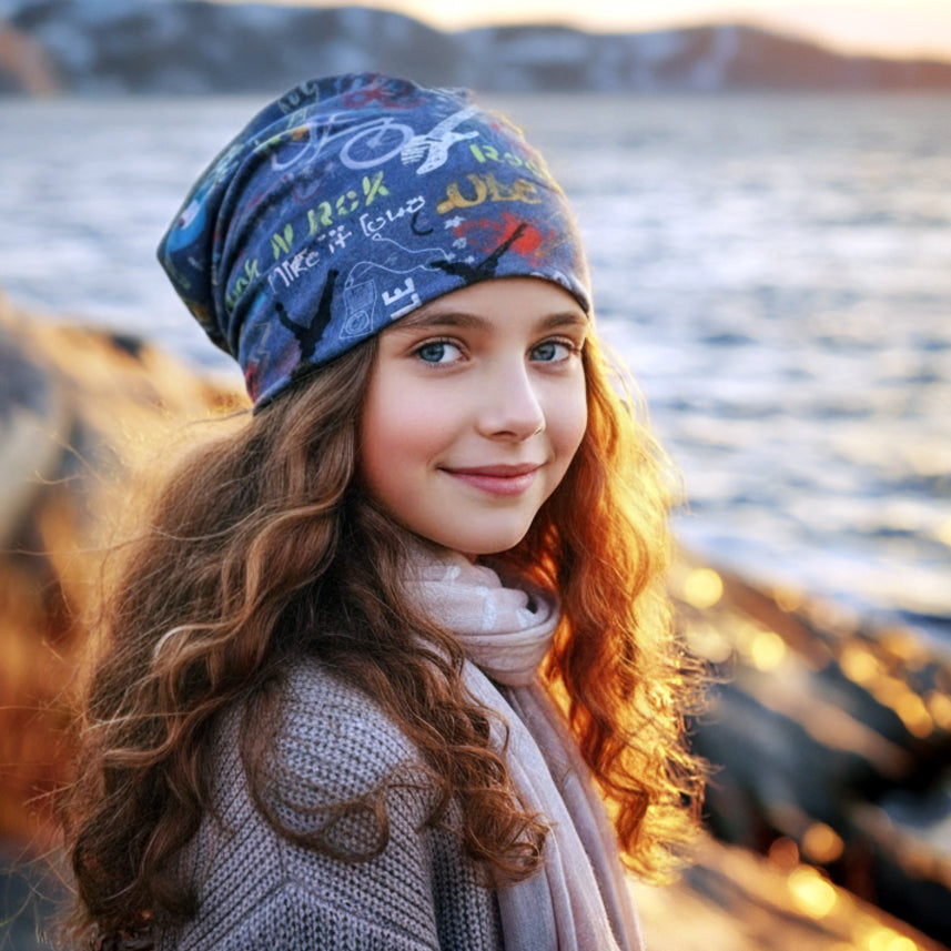 Mädchen am felsigen Ufer trägt Wollhuhn Öko Long Beanie. Handgefertigt, wendbar, bequem und lässig fallend. Ideal für alle Jahreszeiten und milde Wintertage.