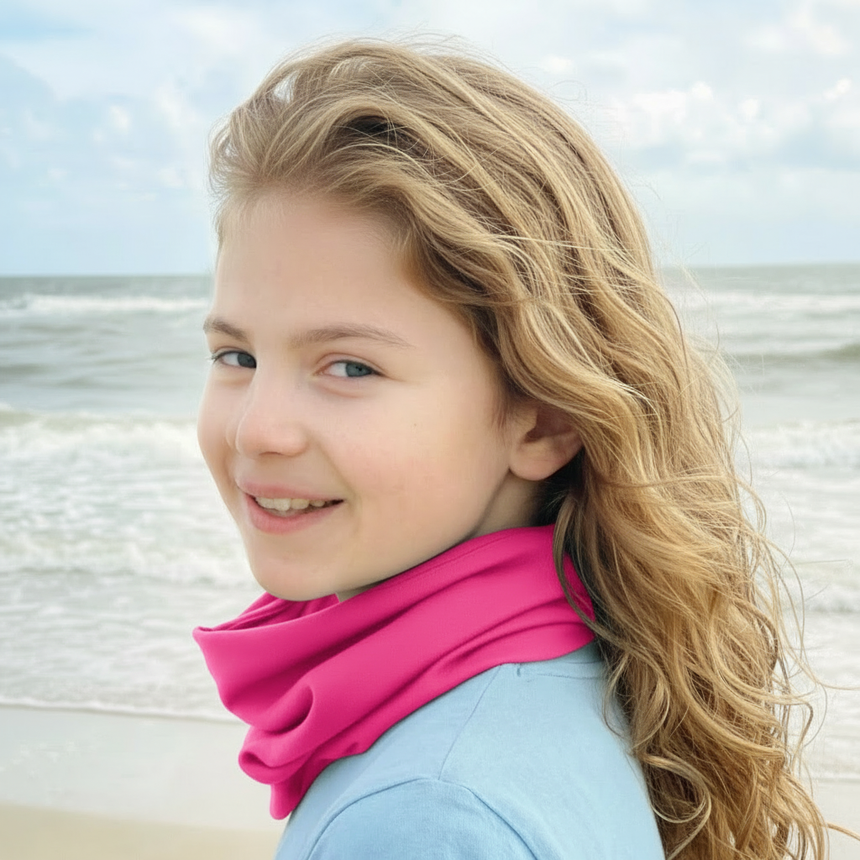 Mädchen am Strand trägt Wollhuhn Leichtes Lockeres Öko Jersey Halstuch in Pink. Handgemachter, weicher Schlupfschal ideal für Übergangszeiten, schützt vor Wind und Sonne.
