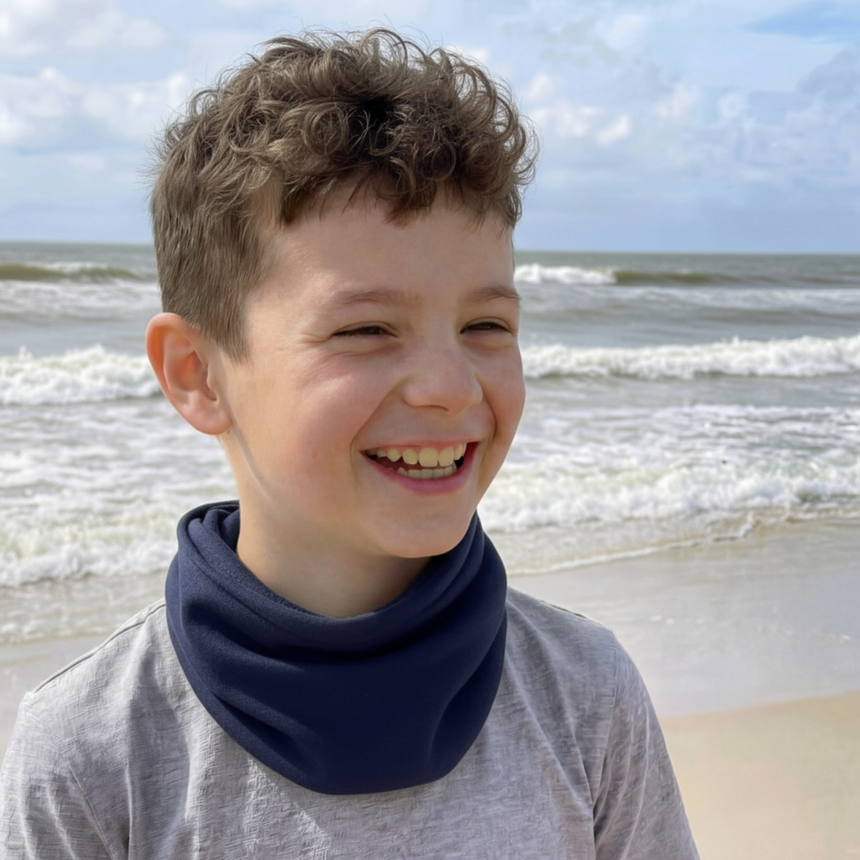 Junge am Strand mit Wollhuhn Leichtes Lockeres Öko Jersey Halstuch in Dunkelblau, lächelnd, zeigt die lockere, bequeme Passform des handgemachten Produkts.