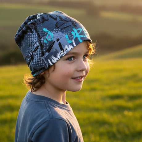 Junge trägt Wollhuhn Öko Shorties, Wendemütze, Ganzjährig, Zweilagig, Skater Blau, in einem Feld bei Dämmerung, lässig und mit leichtem Lächeln.