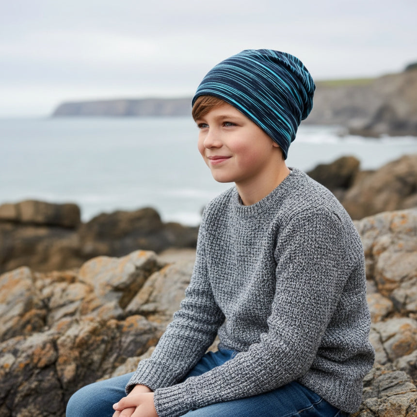 Junge am Meer trägt Wollhuhn Öko Shorties, Wendemütze, zweilagig, ideal für kaltes Wetter, handgefertigt in Deutschland, perfekt für aktive Kinder.