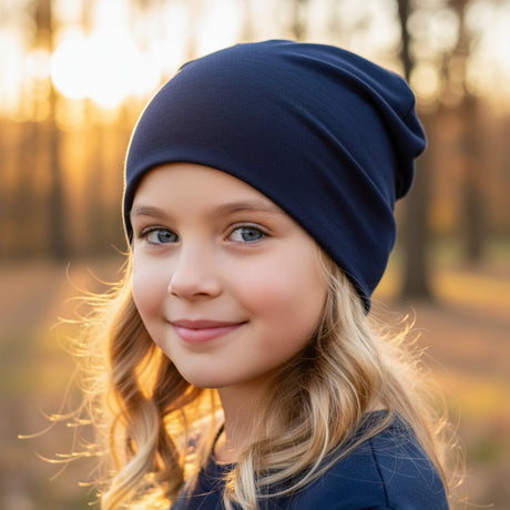 Mädchen mit Wollhuhn Öko Shorties Wendemütze, dunkelblau, im Wald. Handgefertigt, zweilagig, ideal für aktive Kinder, wärmt und wächst mit.