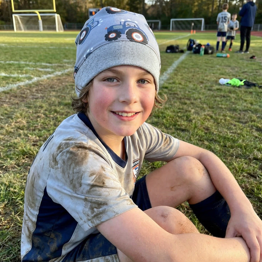 Junge mit Wollhuhn Dünne Öko Beanie-Mütze Sommer/Übergang Einlagig Maxi Traktor/Trecker Grau, nach Fußballtraining sitzend, lächelnd, Mütze handgemacht und sanft zur Haut.