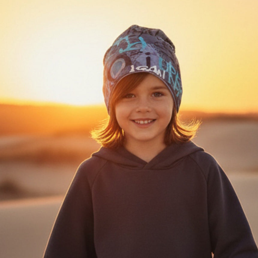 Kind lächelt im Sonnenuntergang, trägt Wollhuhn Öko Long Beanie, zweilagig und wendbar. Perfekt für den lässigen, komfortablen Alltagslook.