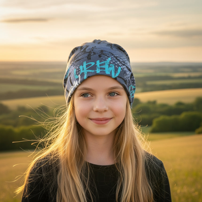 Mädchen trägt Wollhuhn Öko Shorties Wendemütze bei Sonnenuntergang; handgemacht, zweilagig, skaterblau. Perfekt für aktive Kinder, stilvoll und bequem.