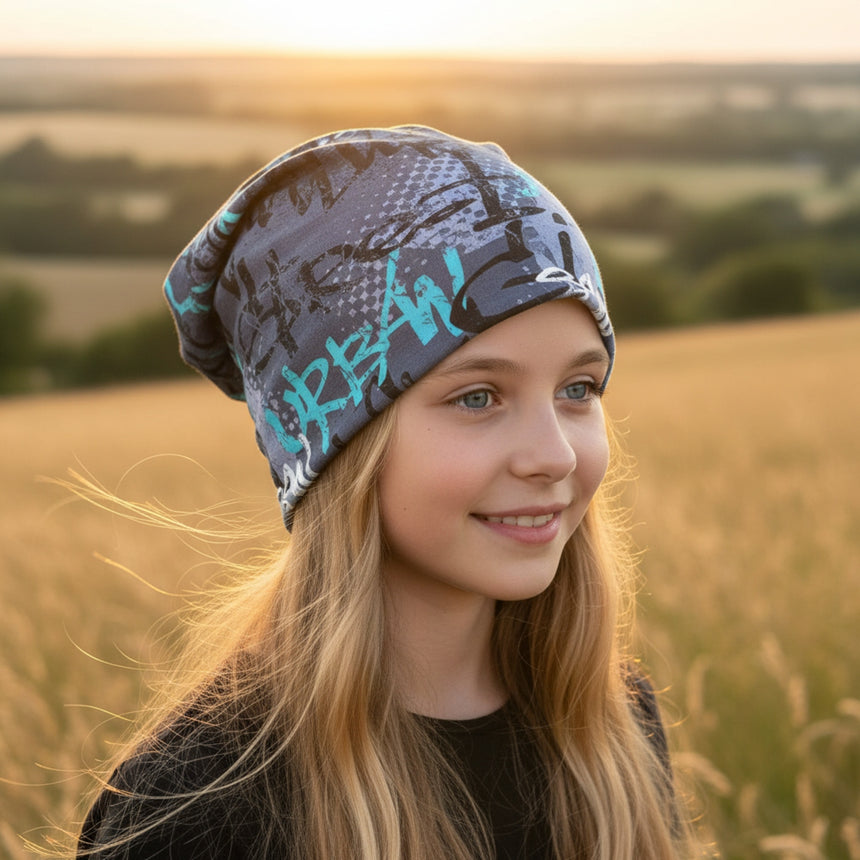 Junges Mädchen trägt Wollhuhn Öko Long Beanie im Graffiti-Design in einem Feld bei Sonnenuntergang, lässig und bequem für alle Jahreszeiten.