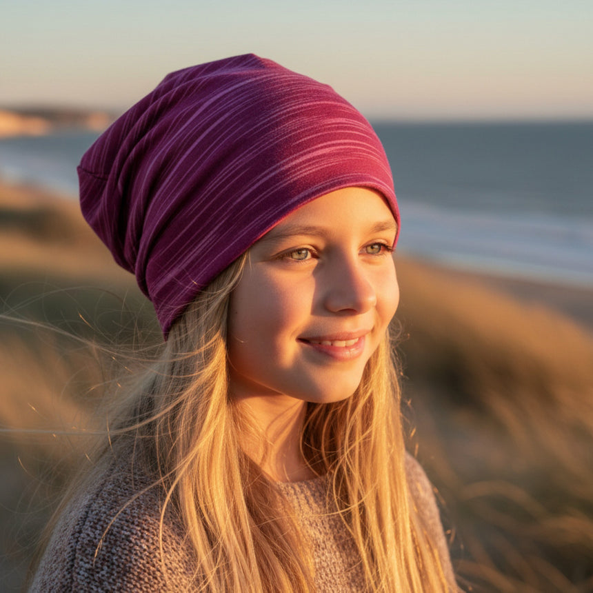 Ein Mädchen trägt die Wollhuhn Öko Long Beanie / Wendemütze, ganzjährig, zweilagig, Lines Beere, auf Sanddünen, lässig im späten Nachmittagslicht.