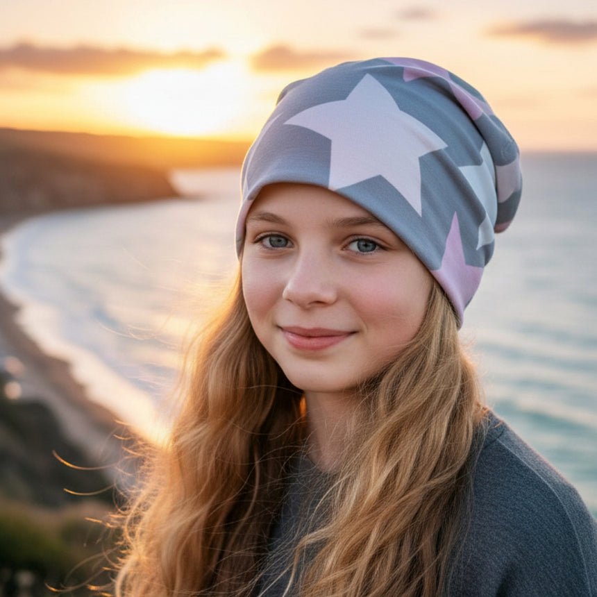 Mädchen mit Wollhuhn Öko Long Beanie, Wendemütze, Big Stars, an einer Meeresklippe bei Sonnenuntergang. Handgemacht, lässiger Look, ideal für alle Jahreszeiten.