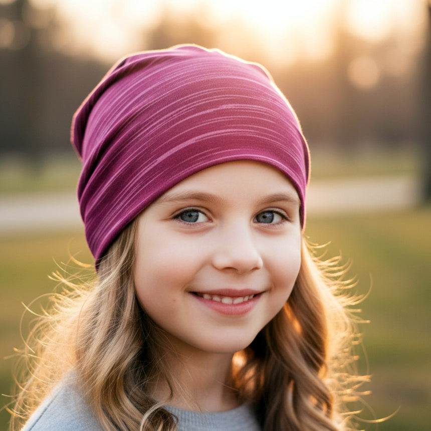 Mädchen trägt Wollhuhn Öko Shorties / Wendemütze, Ganzjährig, Zweilagig, Lines Beere, im Sonnenlicht. Perfekt für aktive Kinder, handgemacht in Deutschland.