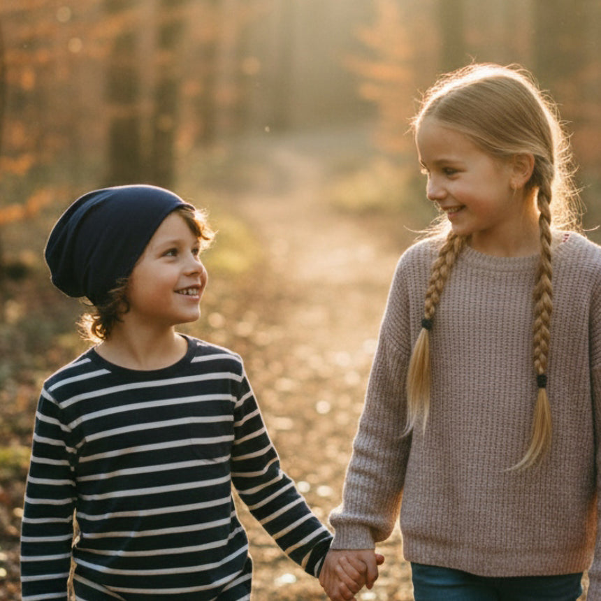 Zwei Kinder spazieren im Herbstwald, das linke trägt die Wollhuhn Öko Long Beanie, dunkelblau, zweilagig, für einen lässigen, komfortablen Look.