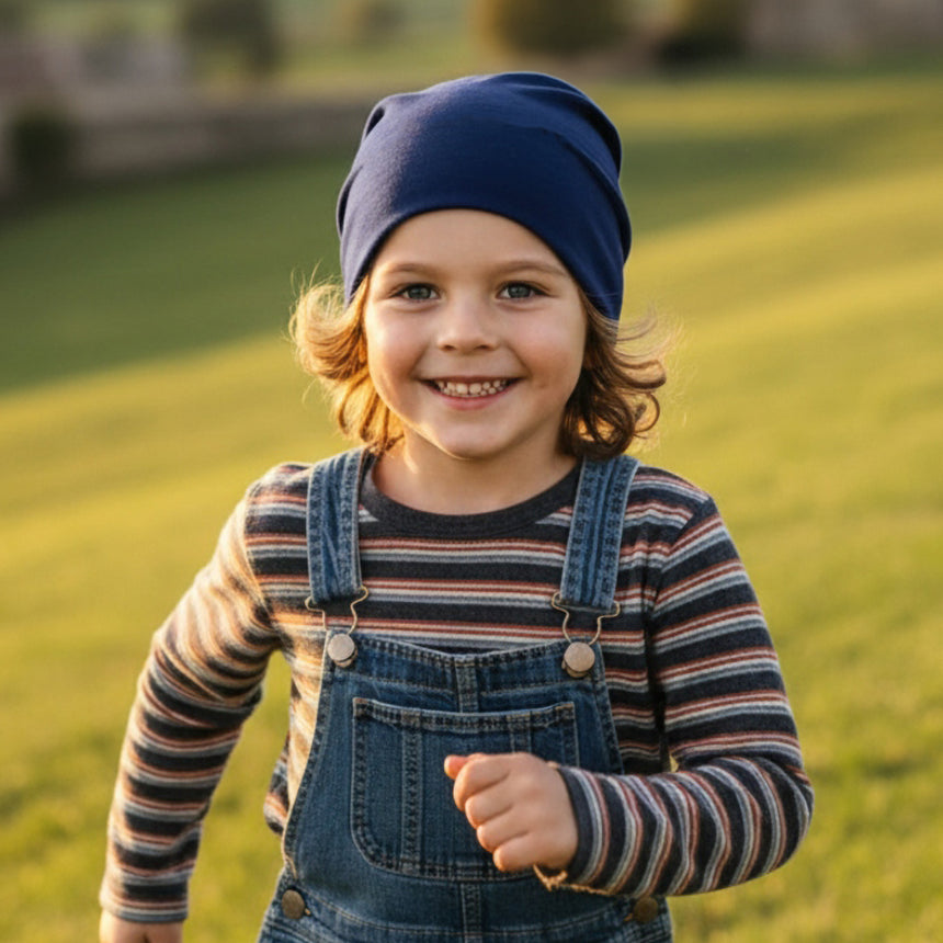 Ein Kind trägt eine Wollhuhn Öko Shorties Wendemütze, während es lächelnd auf einer Wiese läuft. Die Mütze ist zweilagig und einfarbig dunkelblau.