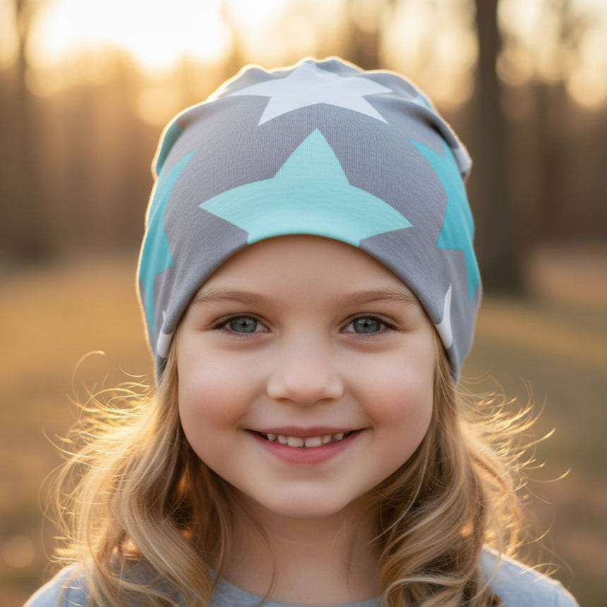 Mädchen trägt eine Wollhuhn Öko Shorties Wendemütze, zweilagig, mit großen grauen und mintfarbenen Sternen, ideal für aktive Kinder.