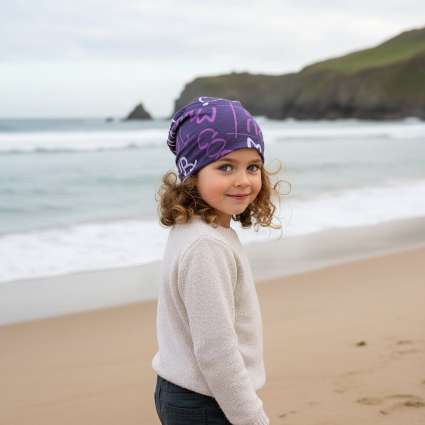 Kind am Strand trägt Wollhuhn Öko Long Beanie in Violett/Beere, zweilagig und wendbar, ideal für Frühling bis milde Wintertage, handgemacht in Deutschland.