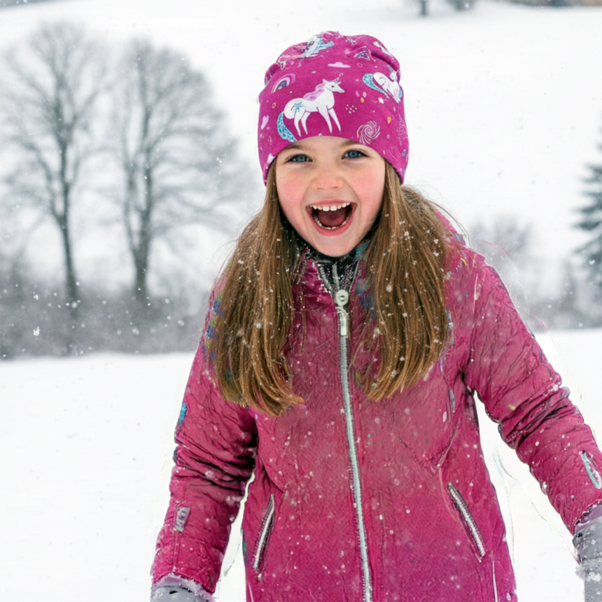 Mädchen in pinkem Einhorn-Muster Wollhuhn Öko Long Beanie, lacht im Schnee. Zweilagig, wendbar, ideal für milde Winter. Handgemacht in Deutschland.