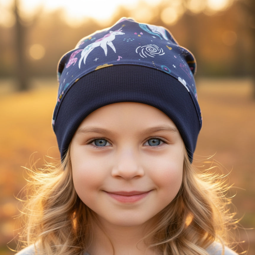 Kind mit blonden Haaren trägt eine Wollhuhn Dünne Öko Beanie-Mütze Sommer/Übergang Einlagig Einhorn/Einhörner Dunkelblau im Park, lächelnd in warmem Herbstlicht.
