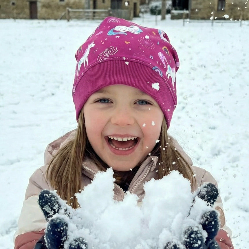 Kind freut sich im Schnee mit Wollhuhn Dünne Öko Beanie-Mütze, Einhornmotiv. Handgemacht, elastisch, ideal für Übergangszeit. Perfekt für aktive Kinder.