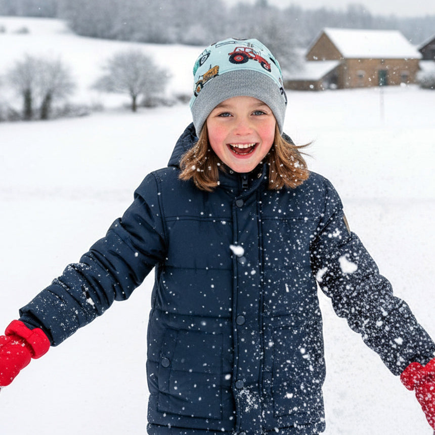 Kind im Schnee mit Wollhuhn Dünne Öko Beanie-Mütze Sommer/Übergang Einlagig Maxi Trecker/Traktor Hellblau, lächelnd und mit ausgestreckten Armen, schneebedeckte Landschaft im Hintergrund.