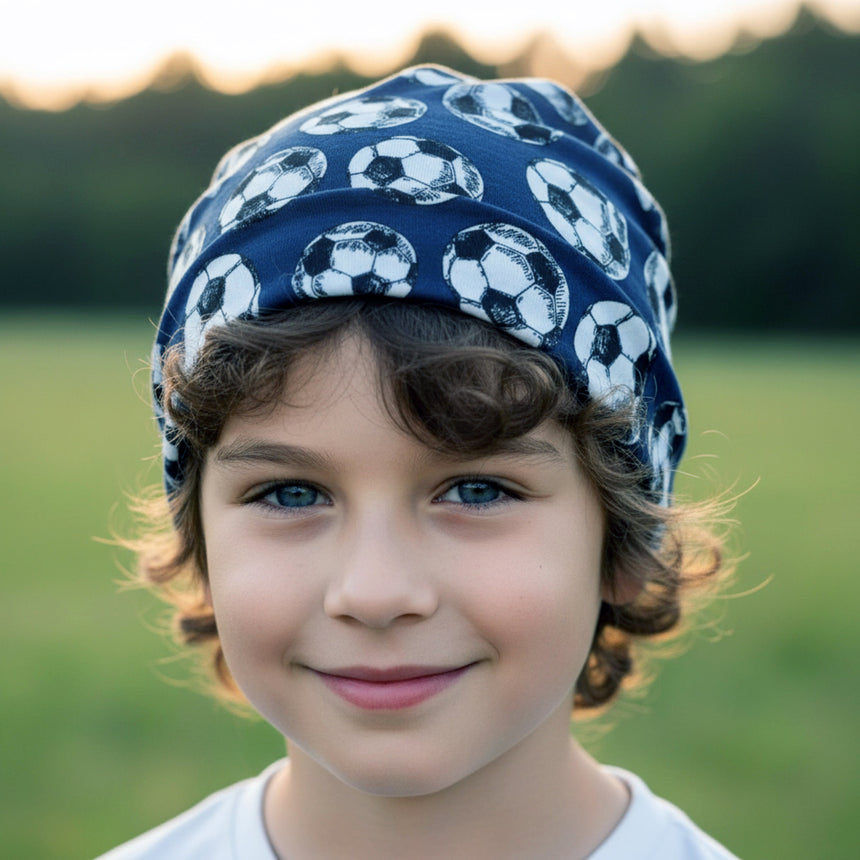 Kind mit Lächeln trägt Wollhuhn Öko Shorties, Fußball Dunkelblau. Handgemachte Wendemütze, ideal für aktive Kinder, bietet komfortable Passform und Schutz bei jedem Wetter.