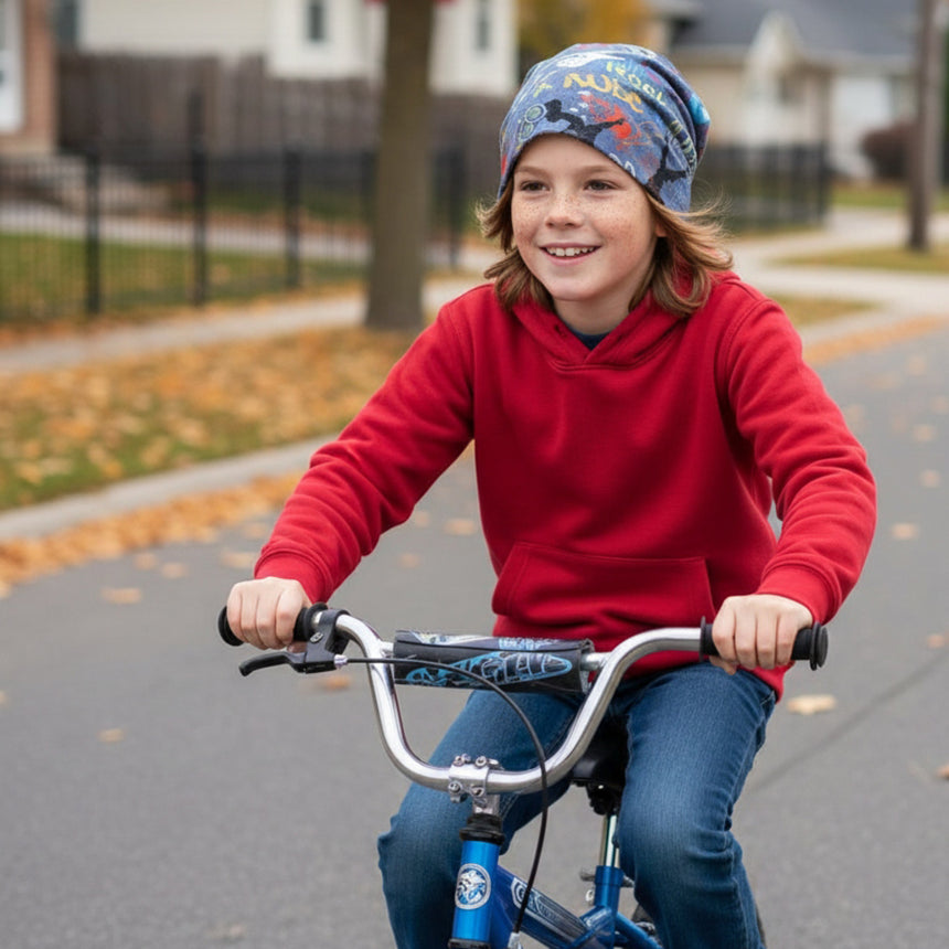 Kind auf Fahrrad trägt Wollhuhn Öko Long Beanie / Wendemütze, Jeansblau, passend unter Helm, ideal für Herbst, handgemacht und bequem, auf ruhiger Vorstadtstraße.