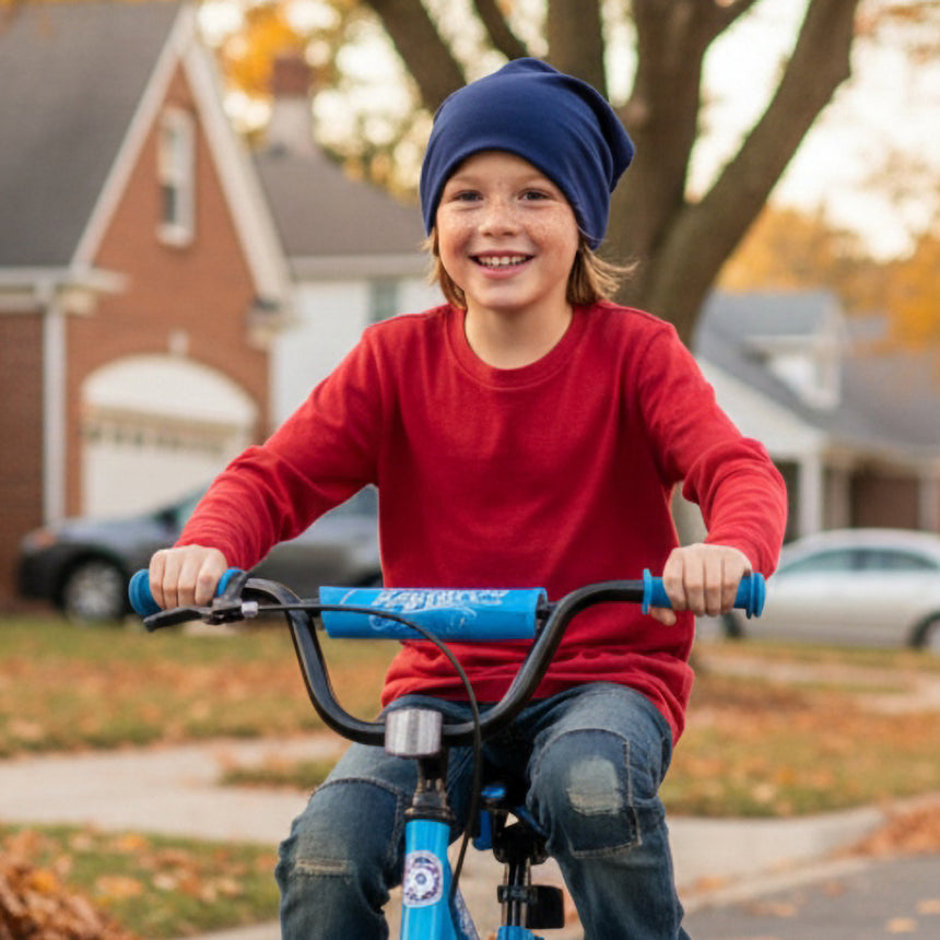 Junge mit Wollhuhn Öko Shorties, Wendemütze, fährt lächelnd Fahrrad; ideal für aktive Kinder, handgemacht, zweilagig, dunkelblau, angenehm dehnbar, unter Helmen tragbar.