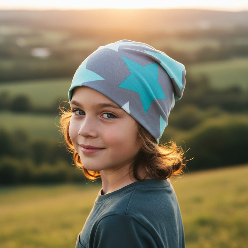 Kind mit Wollhuhn Öko Shorties Wendemütze, grau mit mintfarbenen Sternen, steht im Sonnenuntergang. Handgefertigte, zweilagige Beanie für ganzjährigen Komfort und stilvollen Look.