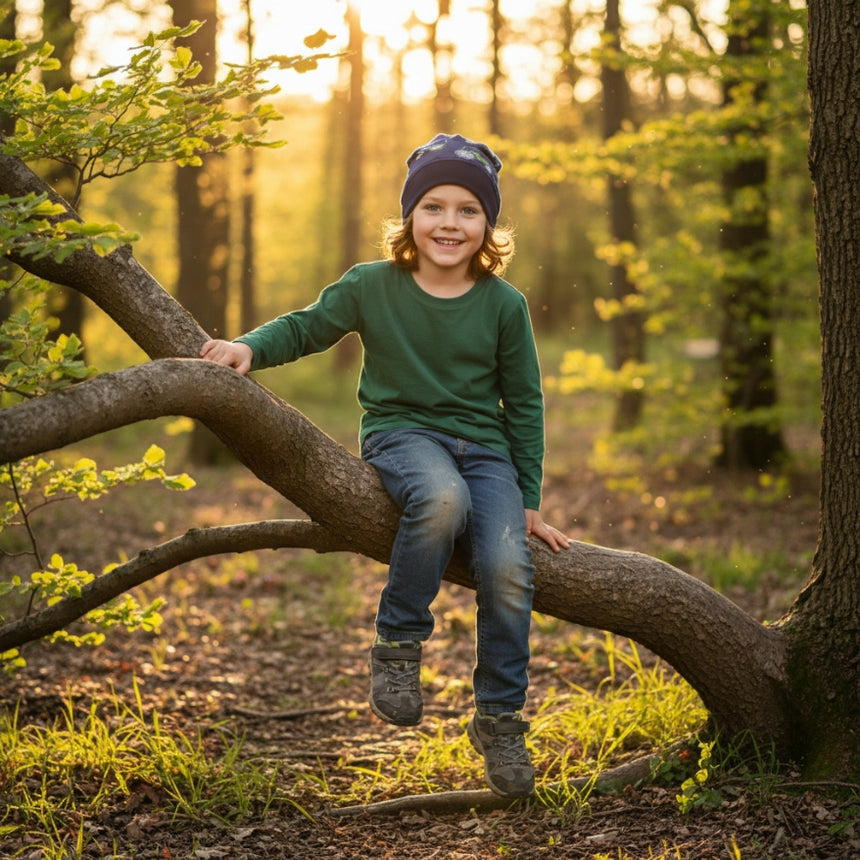Kind sitzt auf Baum in Wald, trägt Wollhuhn Dünne Öko Beanie-Mütze Sommer/Übergang Einlagig, ideal für aktive Kinder, handgemacht und sanft zur Haut.