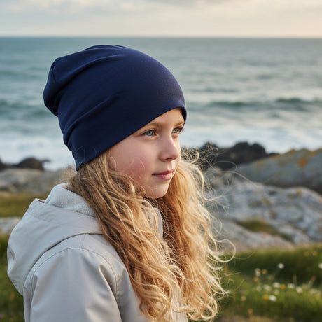 Ein Kind mit blonden Haaren trägt die handgemachte Wollhuhn Öko Long Beanie, wendbar und zweilagig, in Dunkelblau, ideal für ganzjährigen, lässigen Tragekomfort.