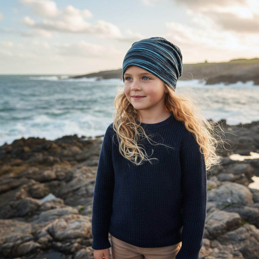 Kind am Meer mit Wollhuhn Öko Shorties Wendemütze, zweilagig, handgemacht; perfekt für aktive Kinder, bietet Komfort und Style.