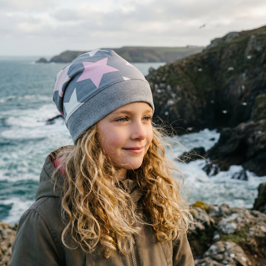Mädchen mit Wollhuhn Dünne Öko Beanie-Mütze Sommer/Übergang Einlagig Big Stars Grau/Rosa/Pink am Felsstrand, ideal für aktive Kinder, handgemacht in Deutschland.