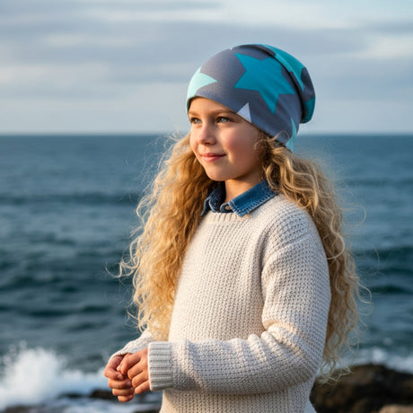 Mädchen am Ufer trägt Wollhuhn Öko Long Beanie, Wendemütze mit großen Sternen, ideal für Kinder, aus weichem, dehnbarem Baumwolljersey, handgefertigt in Deutschland.