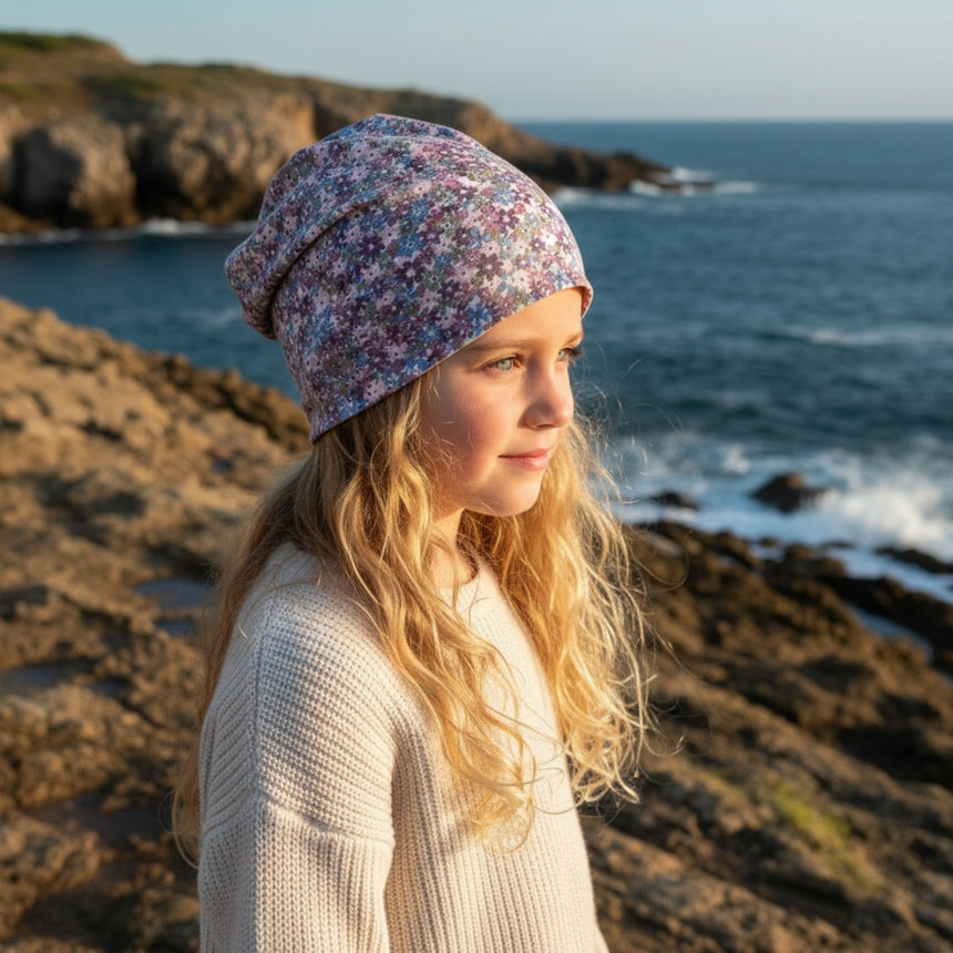 Mädchen am Meer mit Wollhuhn Öko Long Beanie, zweilagig, Blümchen Dark Pastell, aus weichem Baumwolljersey, ideal für ganzjähriges Tragen.