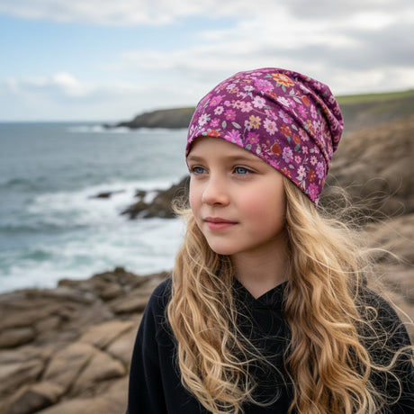 Mädchen am Meer trägt Wollhuhn Öko Shorties / Wendemütze, Ganzjährig, Zweilagig, Blumen Beere. Ideal für aktive Kinder, handgefertigt in Deutschland.