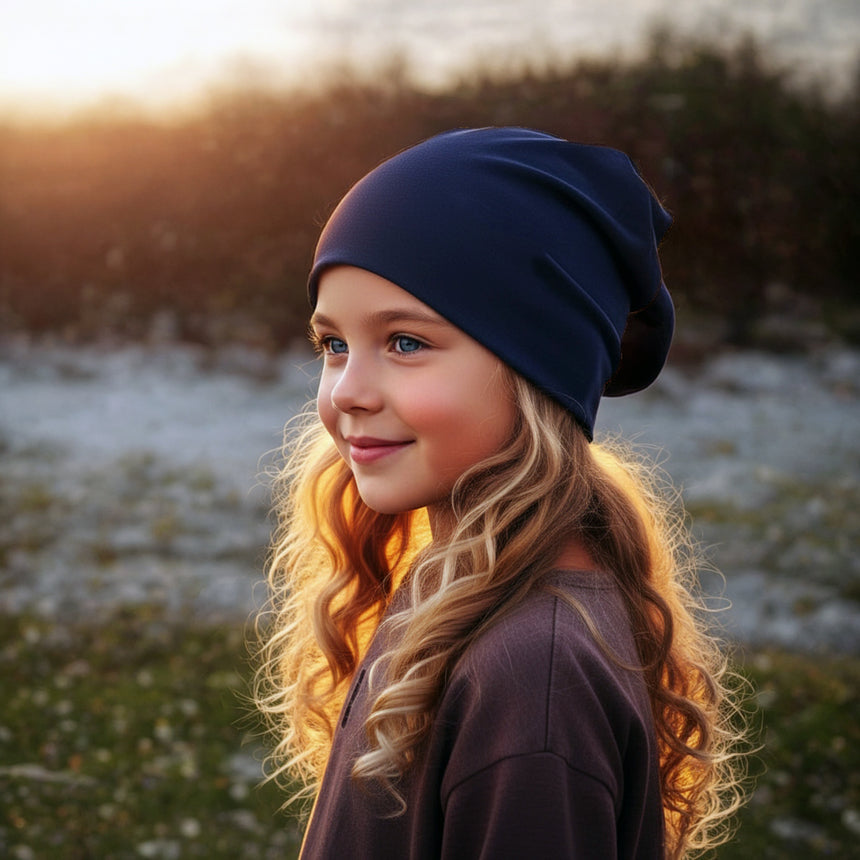 Mädchen mit blonder Mähne trägt Wollhuhn Öko Long Beanie in Dunkelblau, lässig fallend, zeigt optimalen Sitz bei warmem Spätnachmittagslicht im Freien.