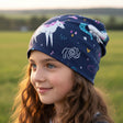 Mädchen mit braunen Haaren trägt Wollhuhn Öko Shorties Wendemütze, zweilagig, mit Einhörnern. Ideal für aktive Kinder, handgemacht in Deutschland.