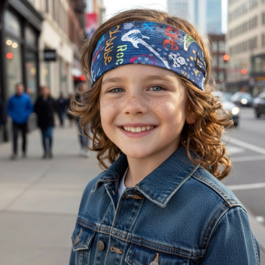 Kind mit blauem Wollhuhn Elastisches Öko Stirnband, verziert mit Gitarrenmotiven, steht lächelnd auf einem Bürgersteig. Stirnband aus Bio-Baumwolle, ideal für Outdoor-Aktivitäten.