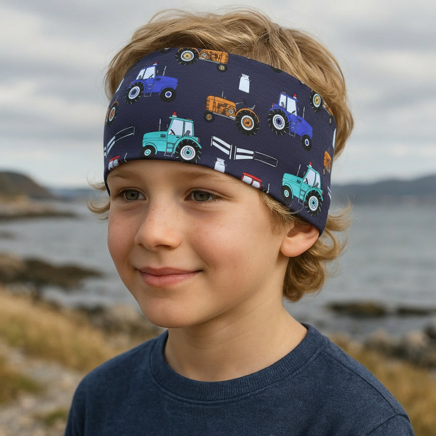 Ein Junge trägt das Wollhuhn Elastisches Öko Stirnband mit Traktormuster in Dunkelblau, ideal für Outdoor-Aktivitäten, handgefertigt aus weicher, atmungsaktiver Bio-Baumwolle.