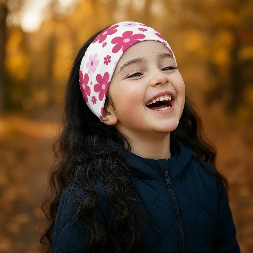 Kind lacht im Freien, trägt Wollhuhn Elastisches Öko Stirnband / Haarband Jersey Zweilagig Blumen Weiß/Pink, ideal für Herbsttage, handgemacht aus Bio-Baumwolle.