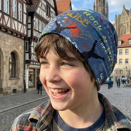 Ein lächelnder Junge trägt eine Wollhuhn Öko Shorties Wendemütze. Die farbenfrohe Beanie ist handgemacht, zweilagig und ideal für aktive Kinder.