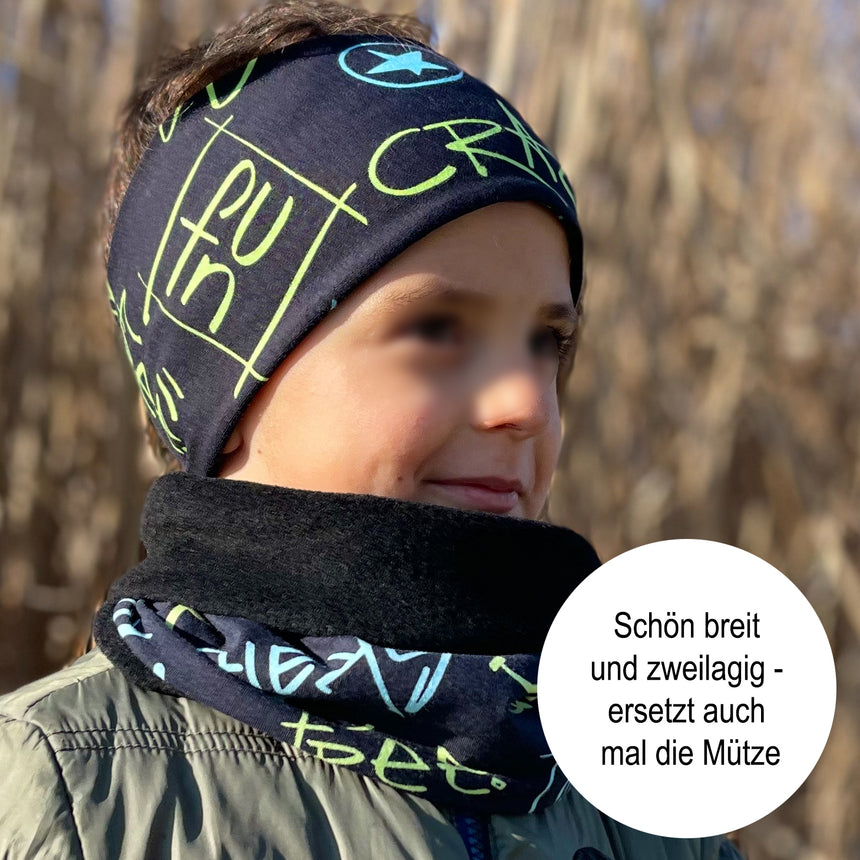 Kind trägt Wollhuhn Elastisches Öko Stirnband / Haarband Jersey Zweilagig Breit Coole Skulls Blau/Schwarz, ideal für Outdoor-Aktivitäten, handgemacht in Deutschland.