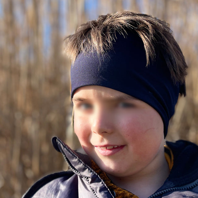 Junge trägt Wollhuhn Elastisches Öko Stirnband/Haarband Jersey Zweilagig Breit Chalk Stars, handgemacht aus weicher, atmungsaktiver Bio-Baumwolle für vielseitige Outdoor-Aktivitäten.
