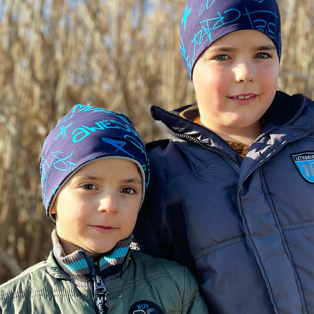 Zwei Jungen tragen die Wollhuhn Öko Long Beanie, eine zweilagige, wendbare Mütze aus weichem Baumwolljersey, ideal für ganzjährigen, komfortablen Schutz.
